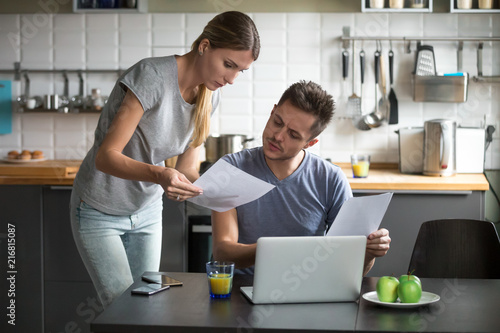 Serious millennial couple worried about high utility bills or rent payment reading papers in kitchen, confused husband and wife discussing bad news in bank loan document having debt financial problem photo