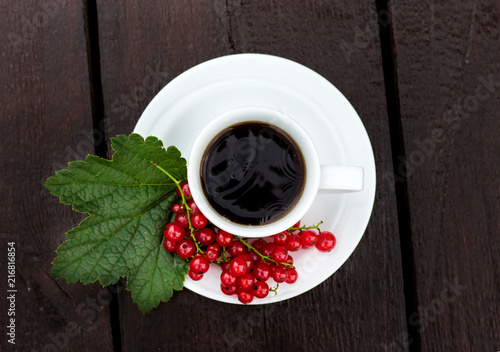 white coffee cup with tea, which on a saucer lay the juicy berries of red currant on a green leaf