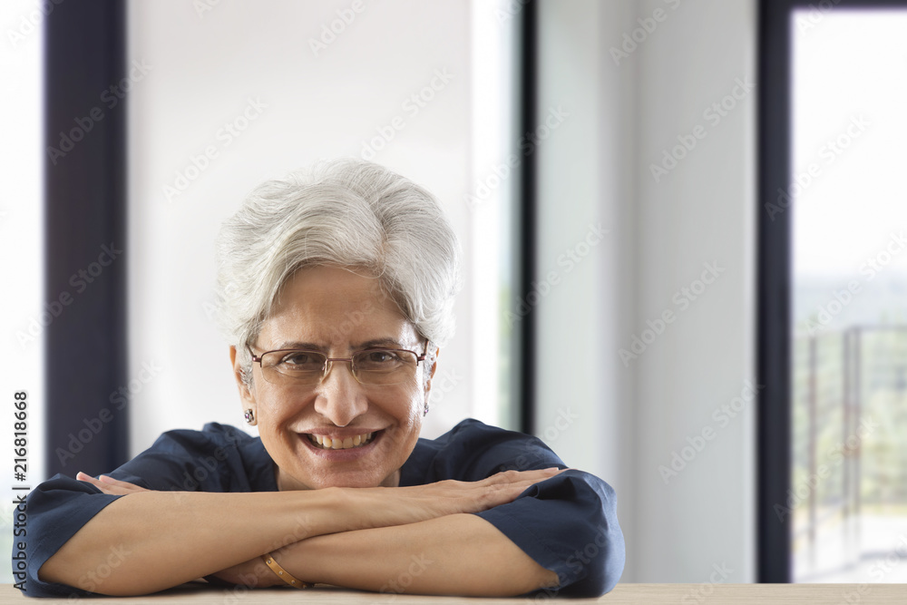 Smiling senior woman leaning on table arms crossed Smiling senior woman leaning on table arms crossed