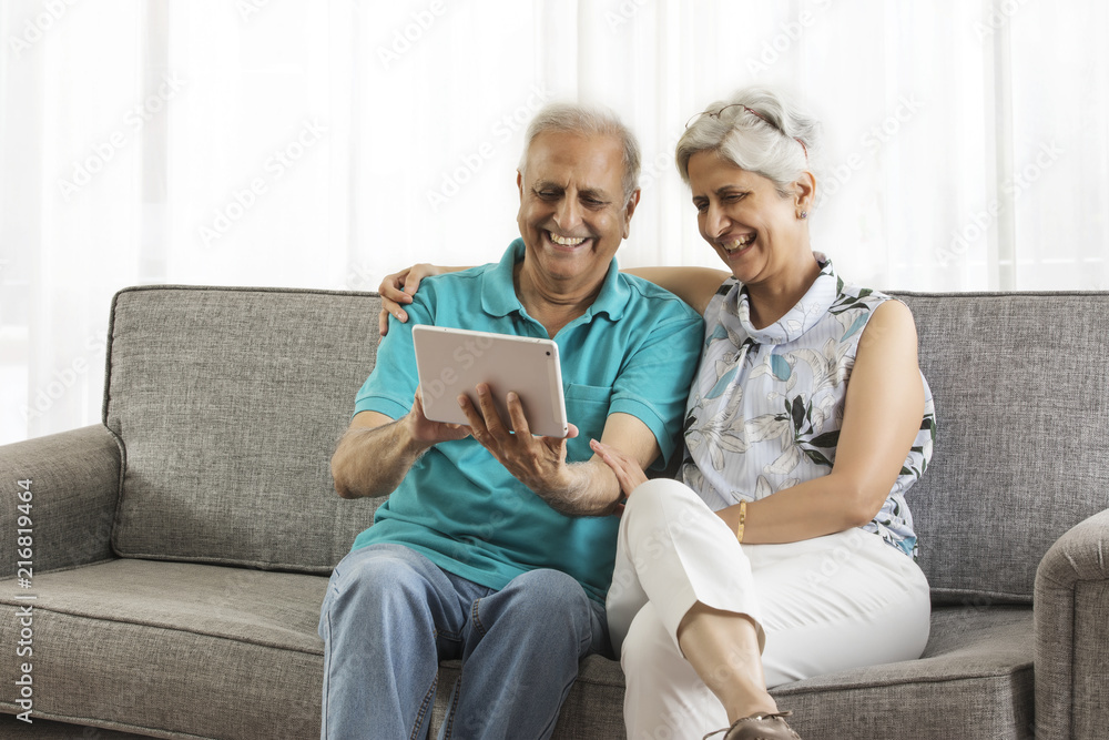 Senior couple sitting on sofa using digital tablet Senior couple sitting on sofa using digital tablet