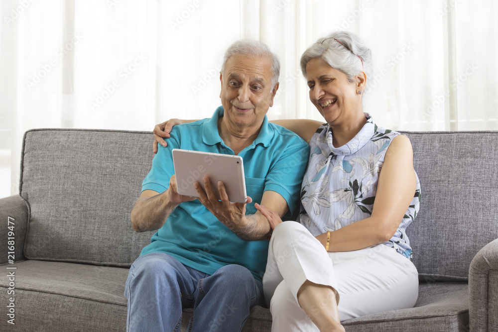 Senior couple using digital tablet sitting on sofa Senior couple using digital tablet sitting on sofa