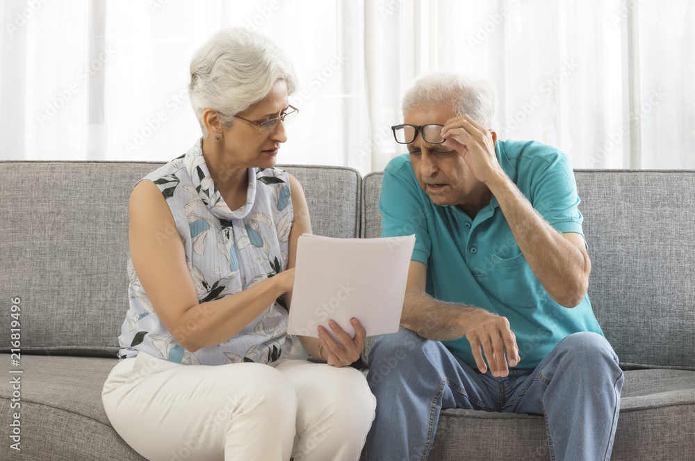 Senior couple looking at document sitting on sofa Senior couple looking at document sitting on sofa