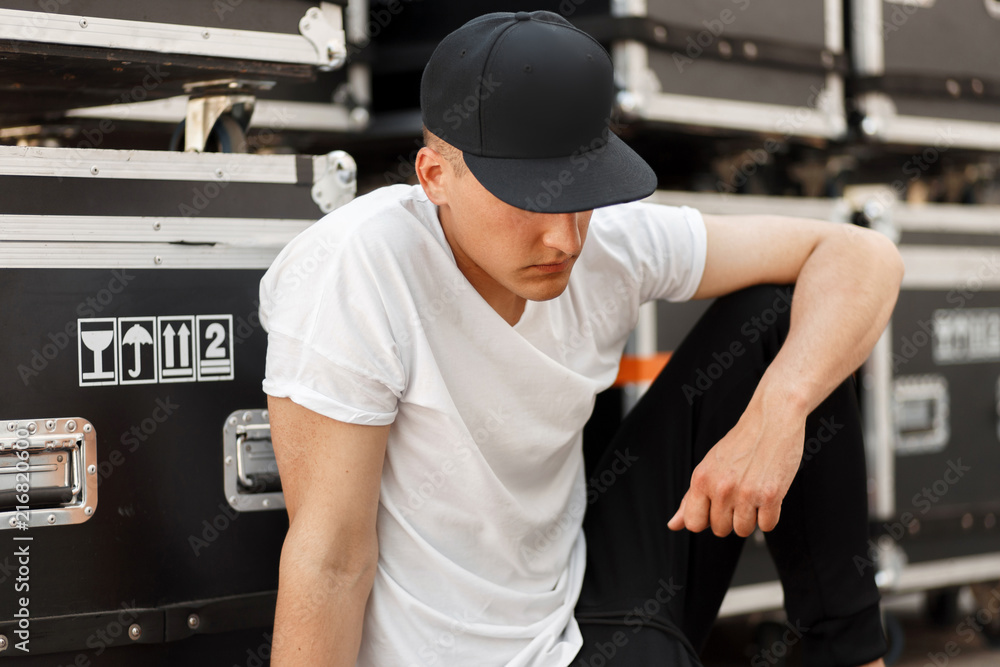 Fashion young man in a fashionable black cap with a stylish white t-shirt  sitting near the boxes Stock Photo | Adobe Stock