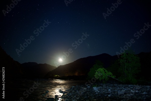 The moon over mountains at night. Wide valley of the river.