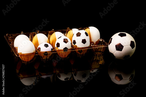 Footballs among the white eggs in the egg tray. Soccer bolls in the egg tray. So there appear soccer balls