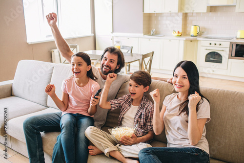 Excited and very happy family is rejoycing. They holds their fists up. Boy has bowl of popcorn. They look happy.