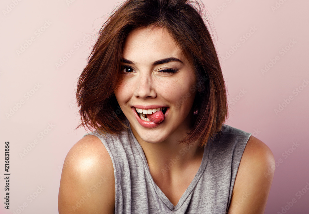 Portrait of beautiful girl showing tongue and winking over pink background. Portrait of beautiful girl showing tongue and winking over pink background.