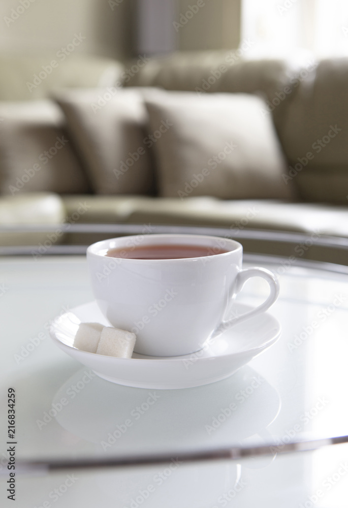 A white cup of tea and a saucer is on a coffee table.