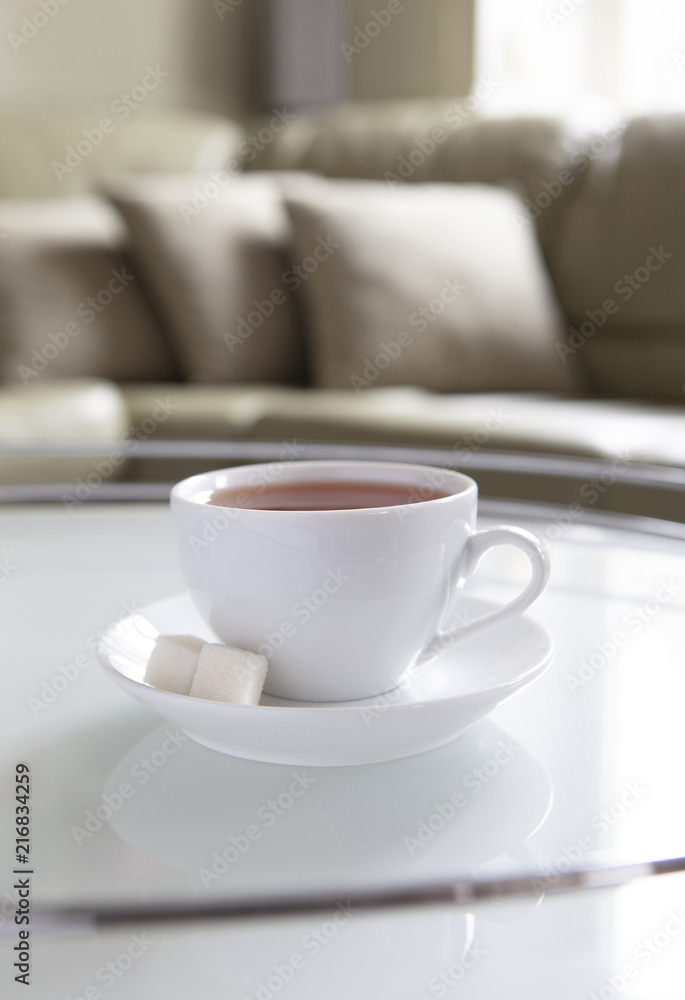 A white cup of tea and a saucer is on a coffee table. A white cup of tea and a saucer is on a coffee table.