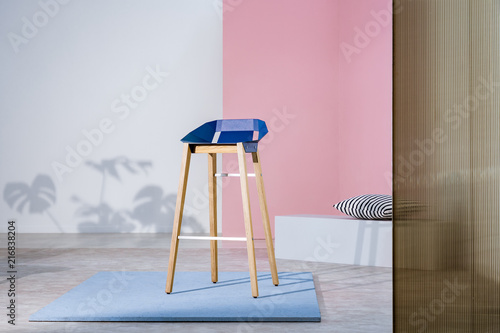 Real photo of an art gallery interior with a blue bar stool with wooden legs on display against pastel pink wall