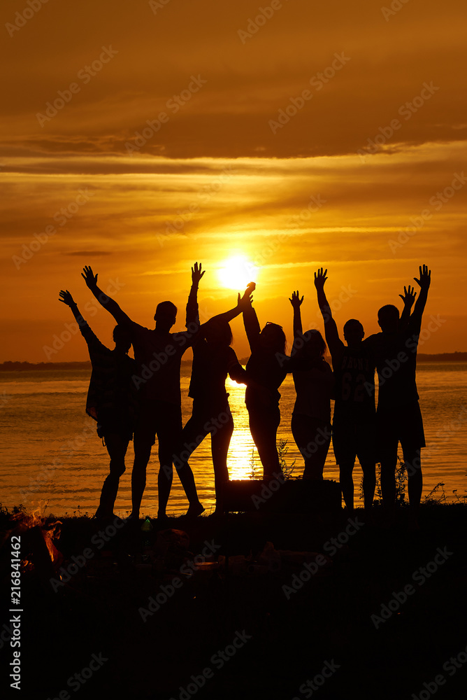Group of happy friends hands up against the sunset.