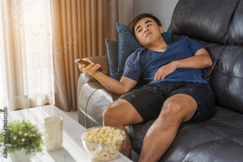 man holding remote control and watching TV while sitting on sofa in the living room photo