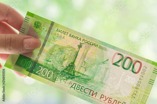 female hand holding new russian banknote against window. two hundred roubles. Cash paper money.