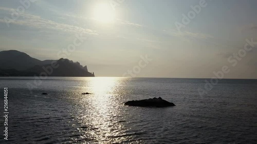 Wallpaper Mural Flying backward over the sea surface with rocks and stones at sunrise. Mountains, rocks, stones in the water and sea waves. Aerial view of Kara Dag Mountain in Crimea. Torontodigital.ca