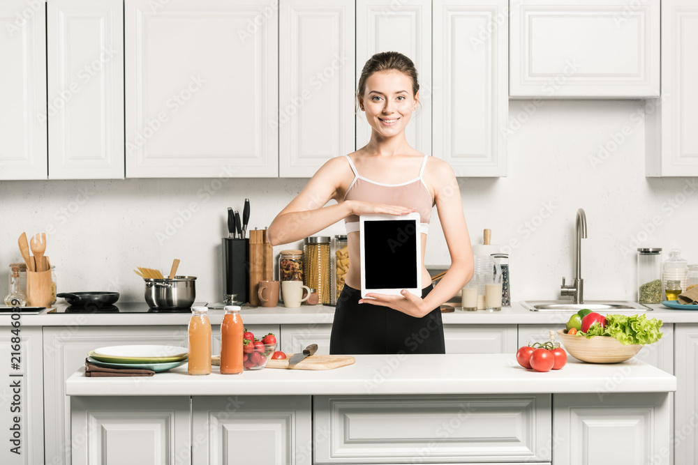 attractive girl in sport bra holding tablet with blank screen in kitchen