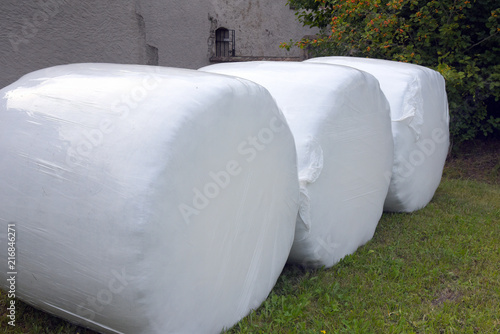 Drei, in weiße Folie verpackte, Heuballen auf einer Wiese photo