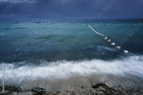 Lubricated small waves with foam during the beginning of the storm in the evening on the shore of the dark sea at the beach of a sea resort photographed for long exposure