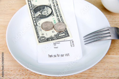 Plate with fork upside down indicating finished with meal, mug beside, bill receipt on plate. For mathematically challenged patrons, double the tax to calculate roughly how to leave for gratuity. photo