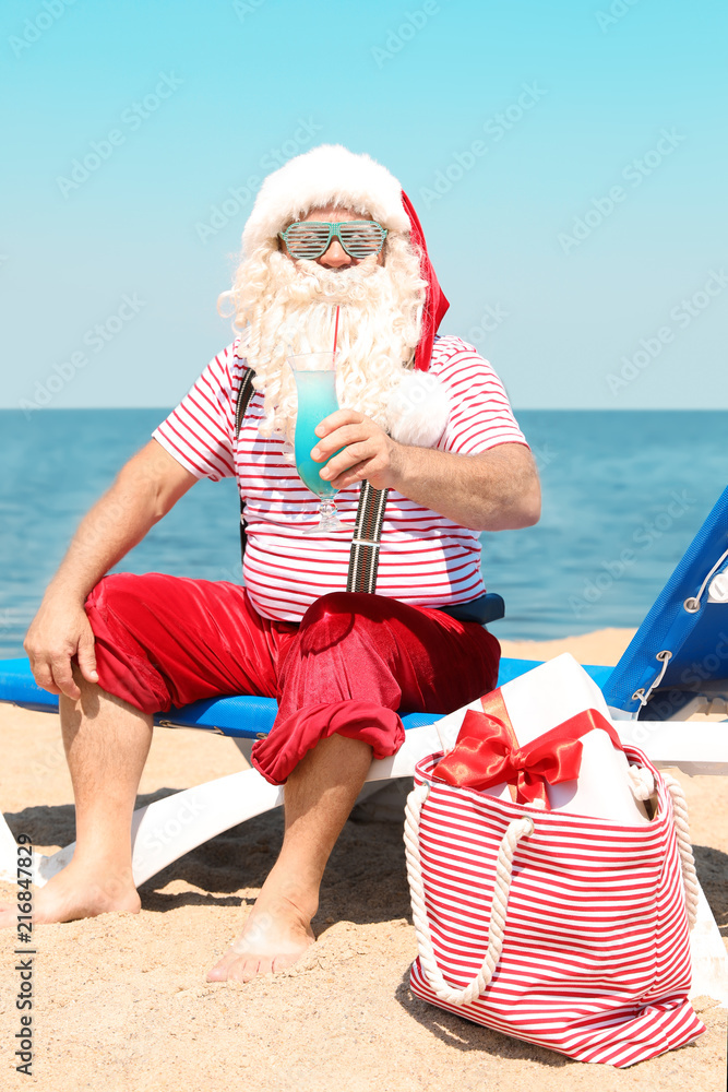 Obraz premium Authentic Santa Claus with cocktail resting on lounge chair at resort