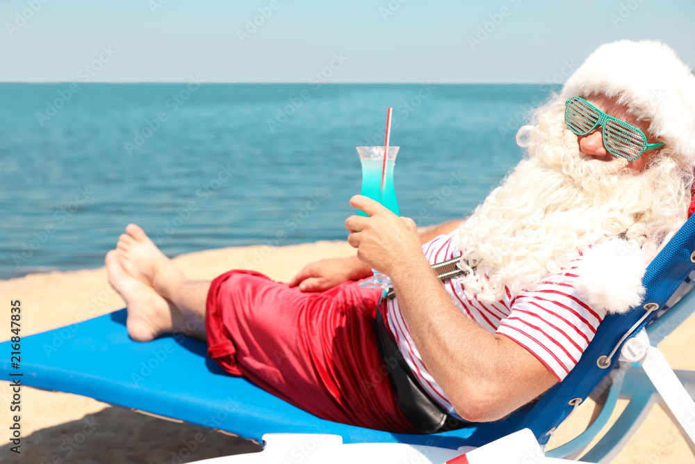 Naklejka premium Authentic Santa Claus with cocktail resting on lounge chair at resort