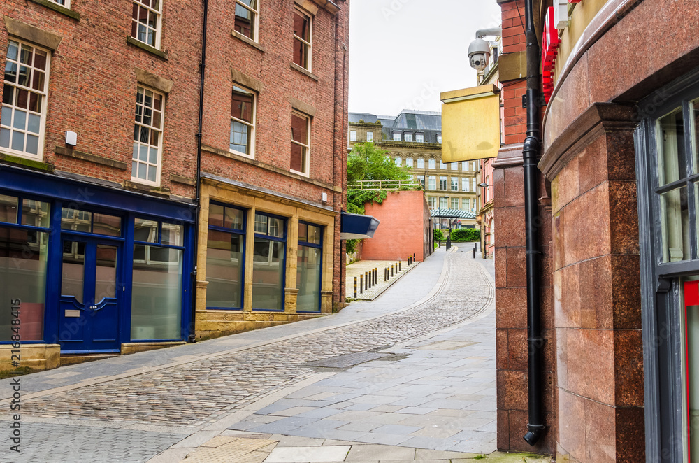 Cobbled Street Lined with Brick Buildings with Colourful Shopfronts in Newcastle upon Tyne on a Cloudy Day