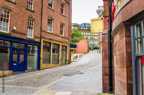Cobbled Street Lined with Brick Buildings with Colourful Shopfronts in Newcastle upon Tyne on a Cloudy Day