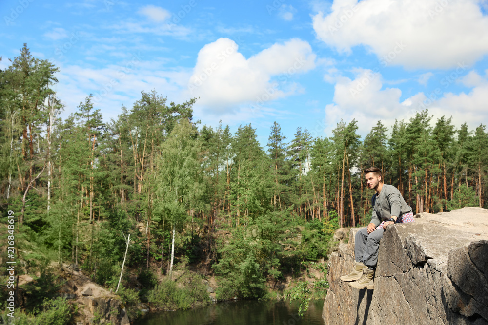 Young man on rock near lake and forest. Camping season Young man on rock near lake and forest. Camping season