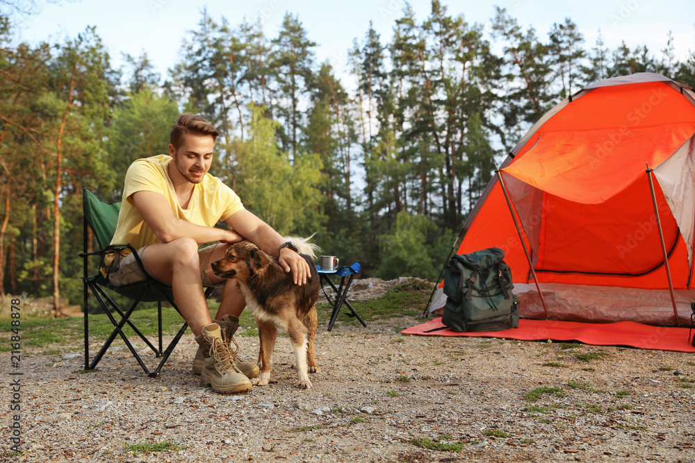 Young man with dog near camping tent outdoors Young man with dog near camping tent outdoors