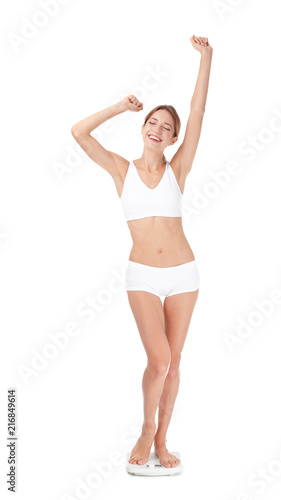 Happy young woman satisfied with her diet results using bathroom scales on white background