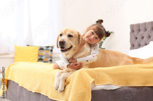 Adorable yellow labrador retriever and little girl on bed at home