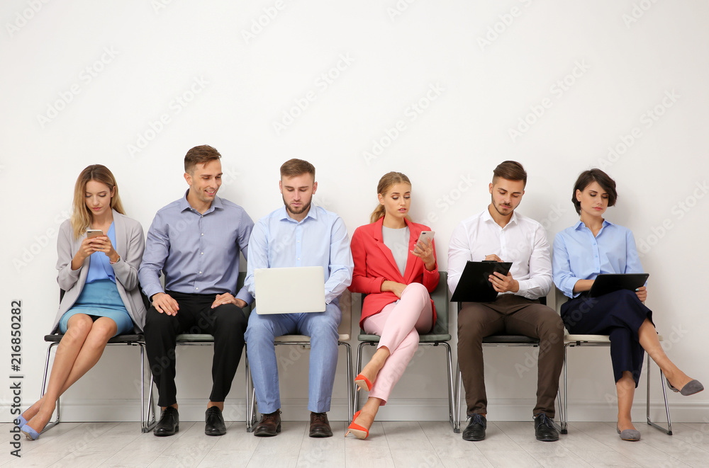 Group of young people waiting for job interview near light wall