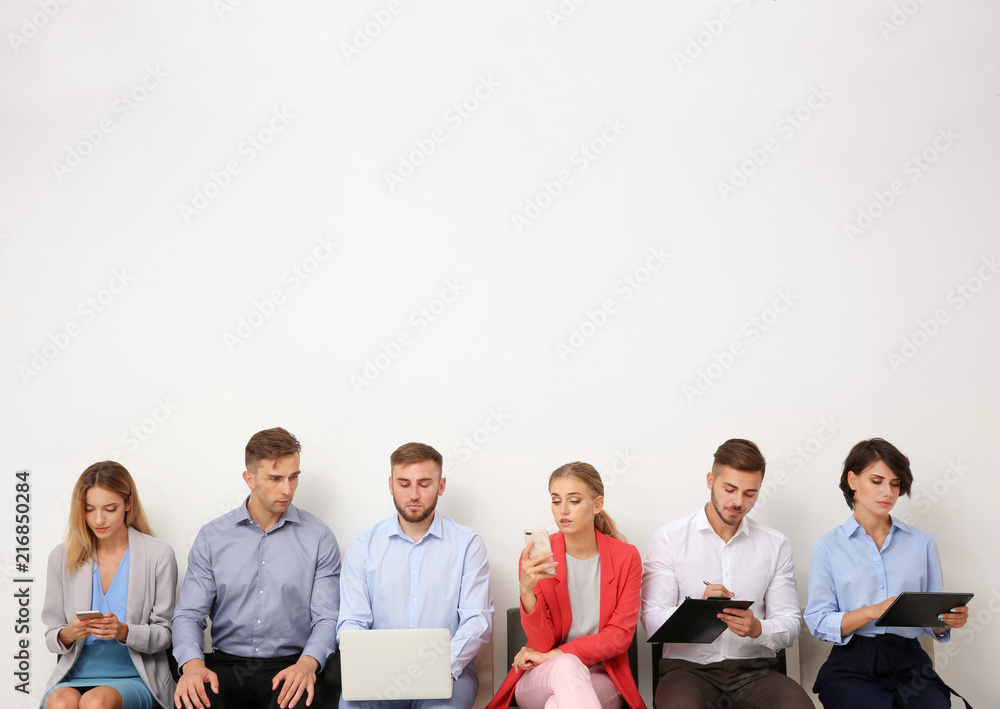 Group of young people waiting for job interview near light wall Group of young people waiting for job interview near light wall