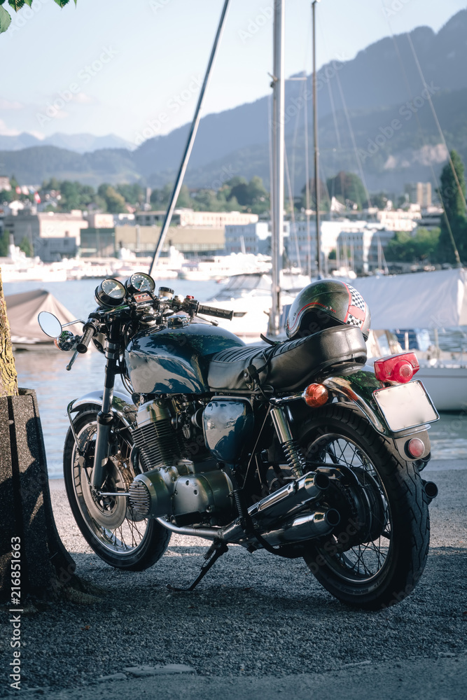 classic style cafe racer motorcycle at sunset time. Bike custom made in vintage. Brutal fun urban lifestyle. pier boats and mountains background