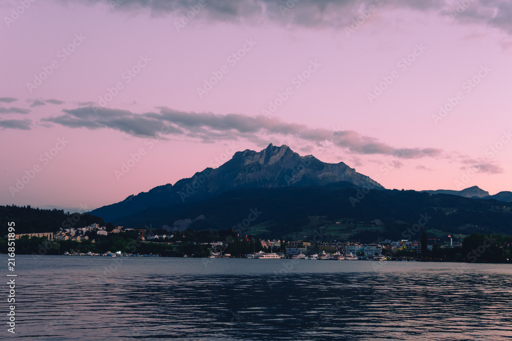 Night summer view with moon light on Alps mountains lake and Pilatus mountain, city glows, travel and vacation in Europe, embankment, Luzern, Switzerland
