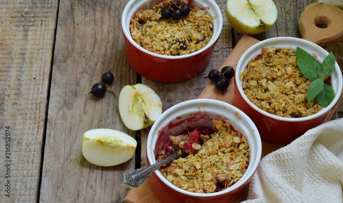 Fruits casserole or crumble with apples and black currant in red cup ramekin. Copy space. Berry and fruits dessert ready to eat. Homemade baking. Healthy pastries. Rustic photo