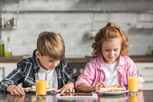 little brother and sister using tablet during breakfast at kitchen