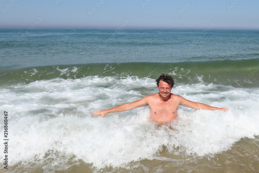 man bathes on the beach as ocean waves crash behind him
