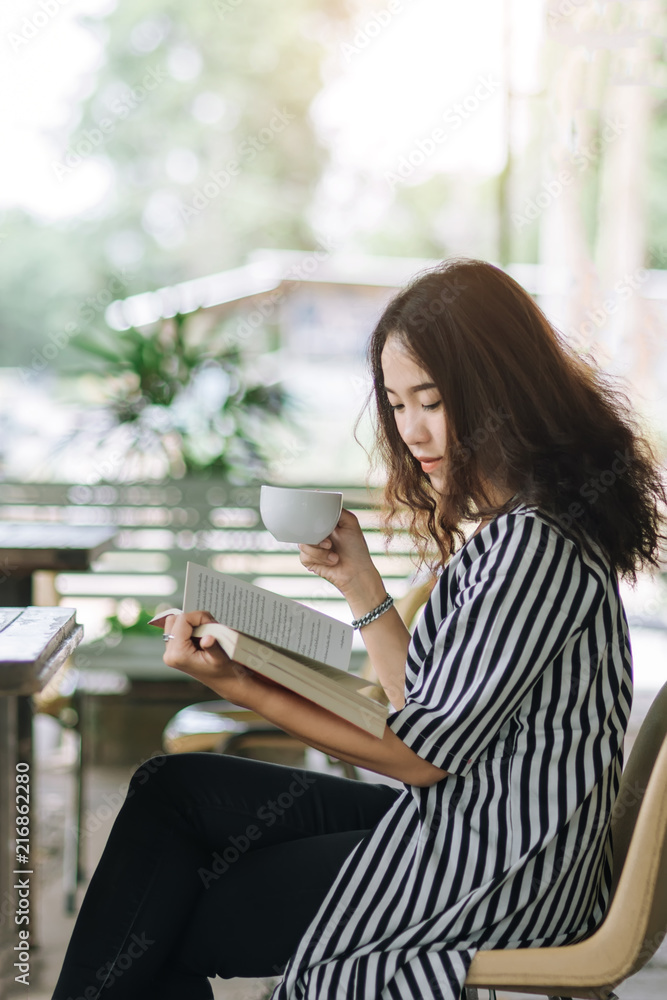 Fototapeta premium Young pretty business woman reading book and enjoy coffee in coffee shop in free time