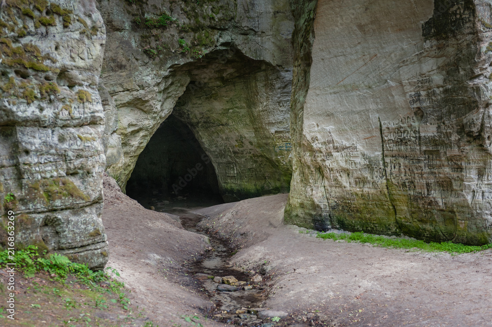 Natural cave in sandstone rock. Entrance to the cave called Little Hell in the Gauja National Park, Latvia. Natural cave in sandstone rock. Entrance to the cave called Little Hell in the Gauja National Park, Latvia.