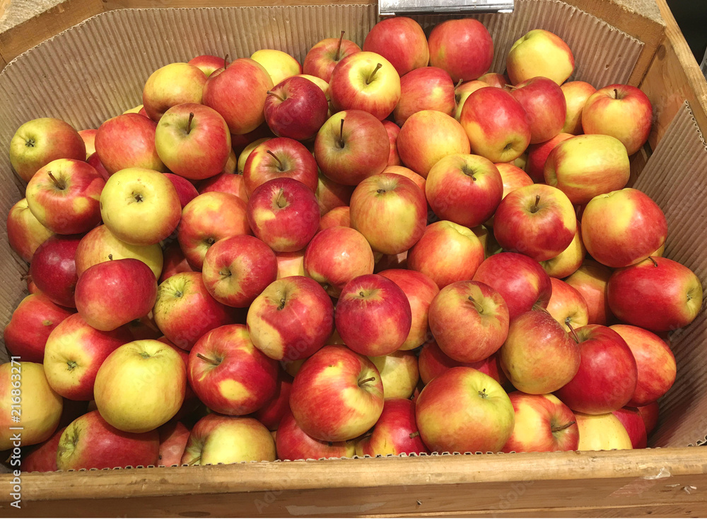 a lot of red apples in wooden box and brown paper in supermaket for sell.