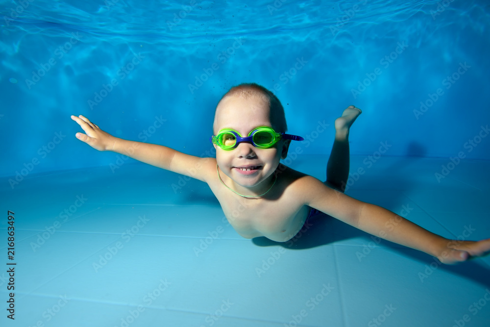 A little boy is lying and posing underwater at the bottom of the pool ...