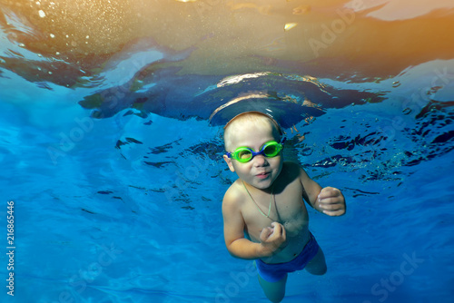 A little boy swims and poses under the water in the children's pool on the background of yellow lights. Portrait. Underwater photography. The horizontal orientation of the image