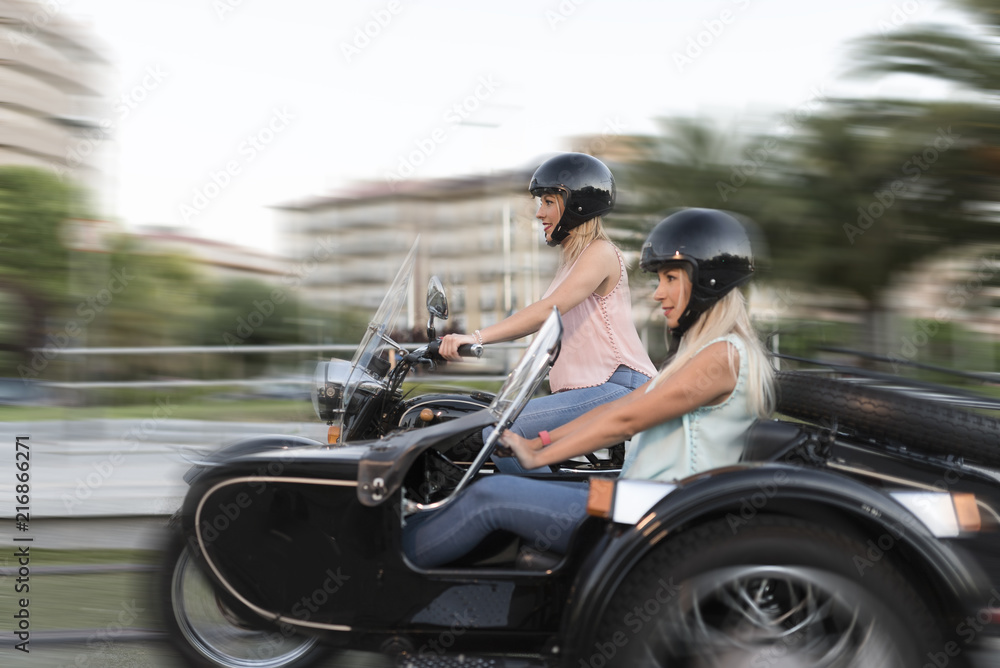 Two happy sister blonde women on sidecar bike smiling and happy Two happy sister blonde women on sidecar bike smiling and happy