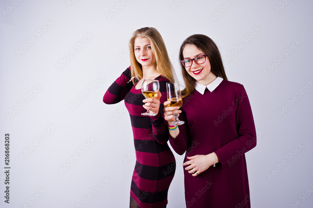 Two attractive friends in purple dresses drink sparkling wine or champagne in the studio. Two attractive friends in purple dresses drink sparkling wine or champagne in the studio.