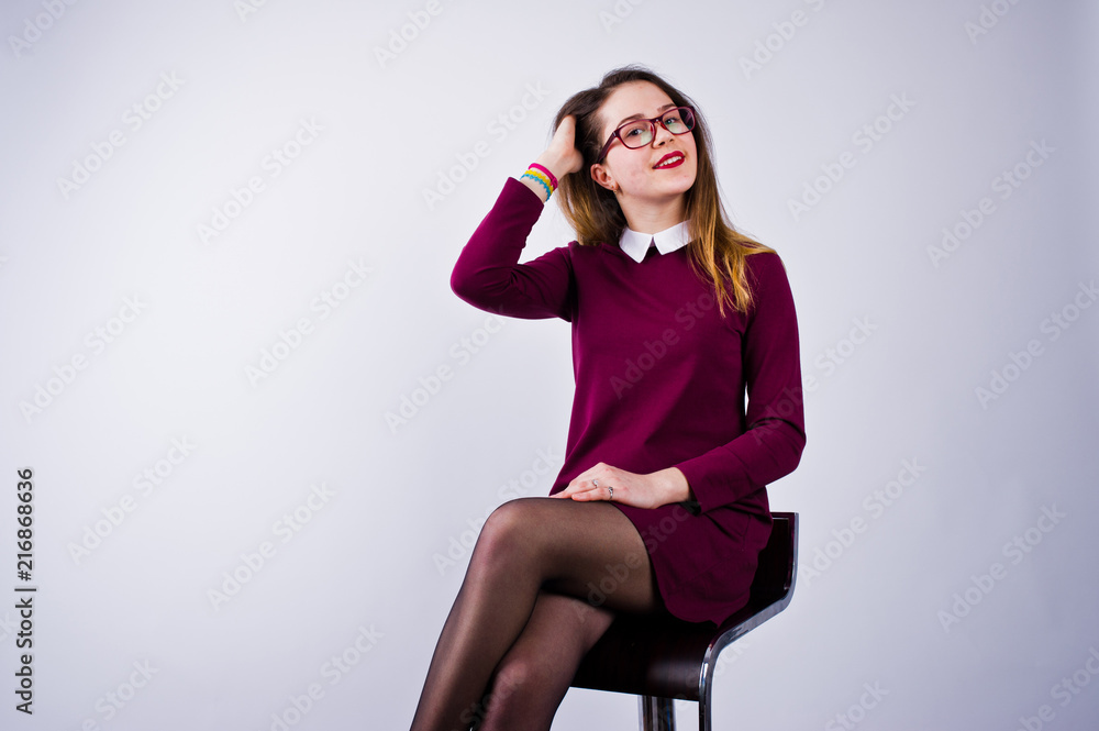 Portrait of a young woman in purple dress and glasses sitting on the chair in the studio. Portrait of a young woman in purple dress and glasses sitting on the chair in the studio.