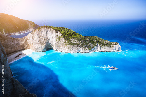 Navagio beach, Zakynthos island, Greece. Tourist trip boat leaving Shipwreck bay with deep turquoise water and white sand beach surrounded by bizarre cliff rocks. Famous landmark location photo
