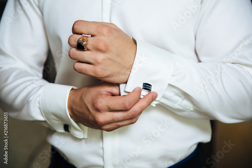 A man in a business suit, white shirt close-up of a cropped frame. The businessman puts on cufflinks, wears a gold finger ring on his finger, an expensive leather belt.