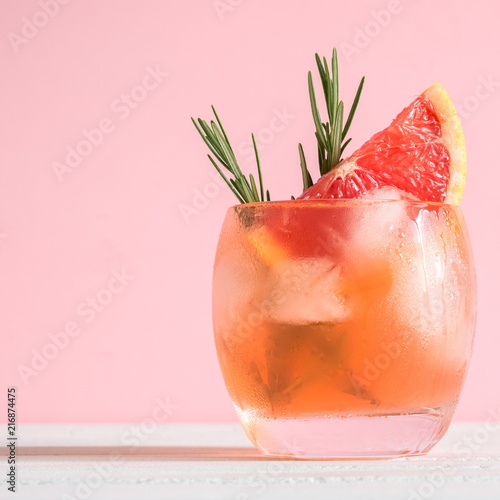 Cold cocktail of grapefruit juice with ice, rosemary, slices citrus on pink background. Space for text. square 
