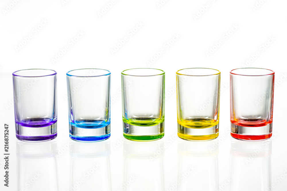 Five multicolored empty shot glasses placed symmetrically on a white background Five multicolored empty shot glasses placed symmetrically on a white background