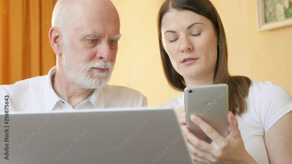 Senior father and his young daughter using cellphone at home. Teen granddaughter teaching grandfather computer literacy, explaining how smartphone works. Active modern life after retirement. Senior father and his young daughter using cellphone at home. Teen granddaughter teaching grandfather computer literacy, explaining how smartphone works. Active modern life after retirement.